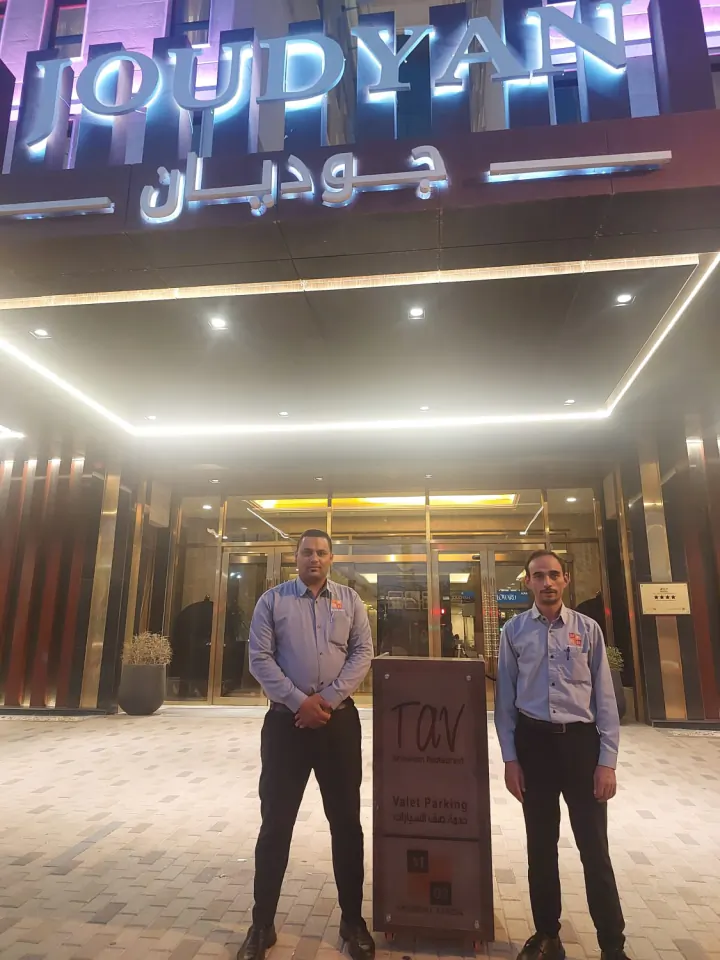 فريق مسارات مدى أمام مدخل جوديان ليلاً مع لوحة خدمة الفاليه